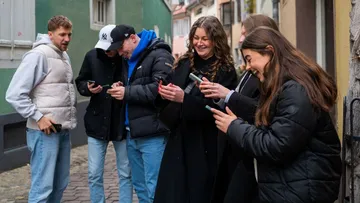Group of people laughing, looking at phones outdoors.