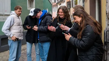 Group of six people using phones outdoors.