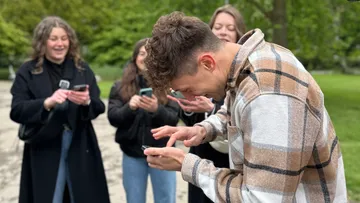 Mann lacht mit Handy, Freunde im Hintergrund.