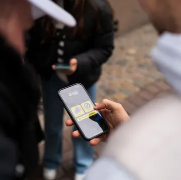 Person nutzt Handy im Freien, zwei andere in der Nähe.