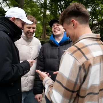 Four friends laughing, looking at phones, outdoors.