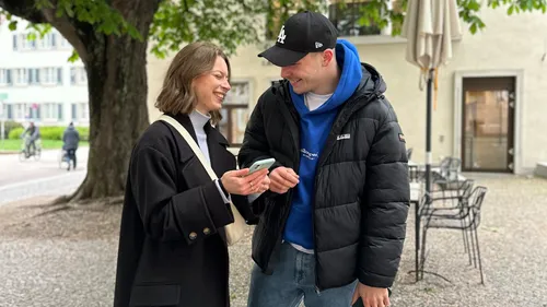 Two people smiling, looking at a phone, outdoors.