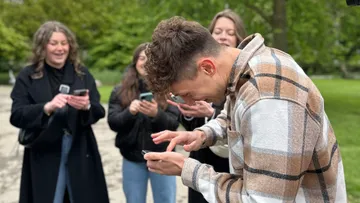 Man laughing with friends using phones outdoors.