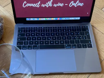 Laptop zeigt „Connect with wine - Online“, Glas daneben.