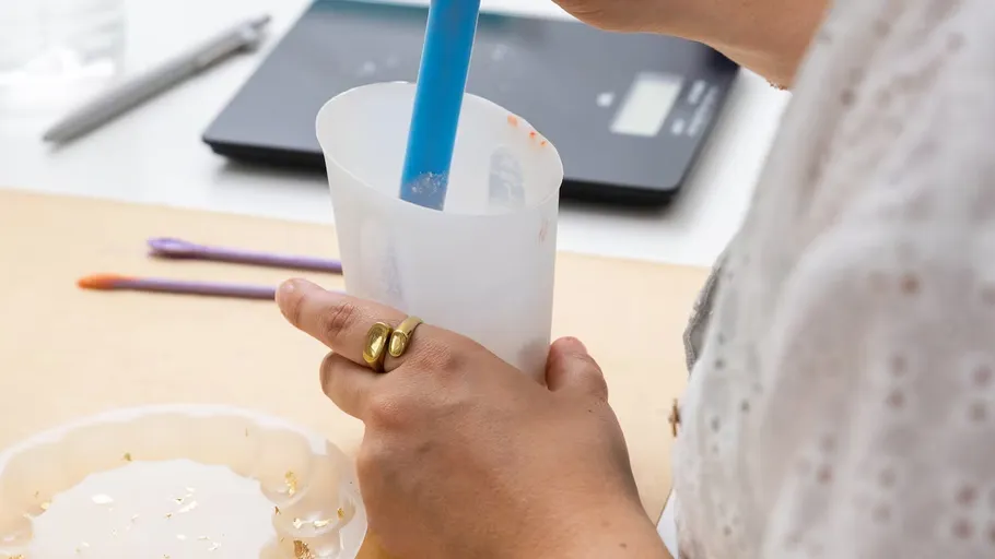 Person stirring resin in a container indoors.