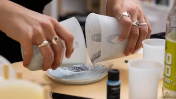 Hands pouring liquid into mold on table.