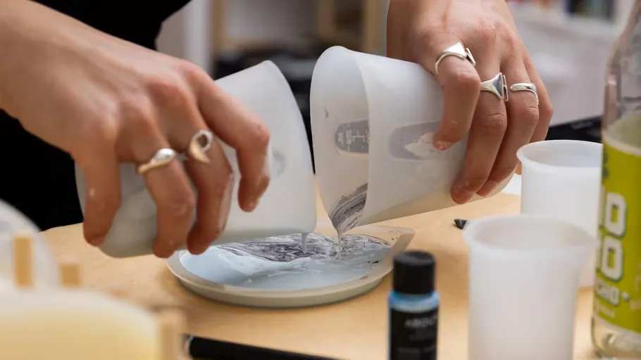 Hands pouring liquid into mold on table.