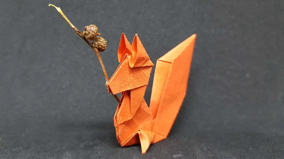 Origami squirrel holding twig on black background.