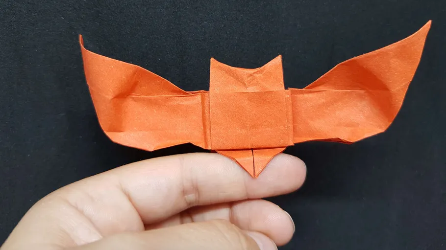 Red origami bat held by fingers.