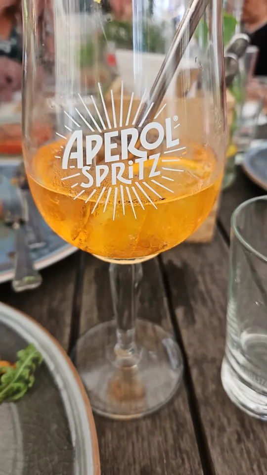 Aperol-Spritz-Glas mit Metallstrohhalm auf Tisch.