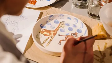 Person painting plate with giraffe design.