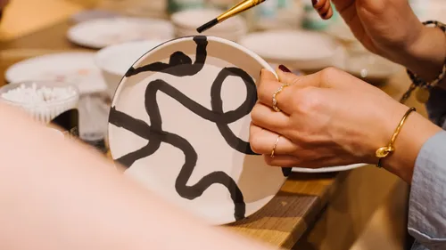 Hands painting black lines on a ceramic plate.