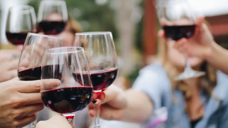 Wine glasses toasting outdoors, people blurred.