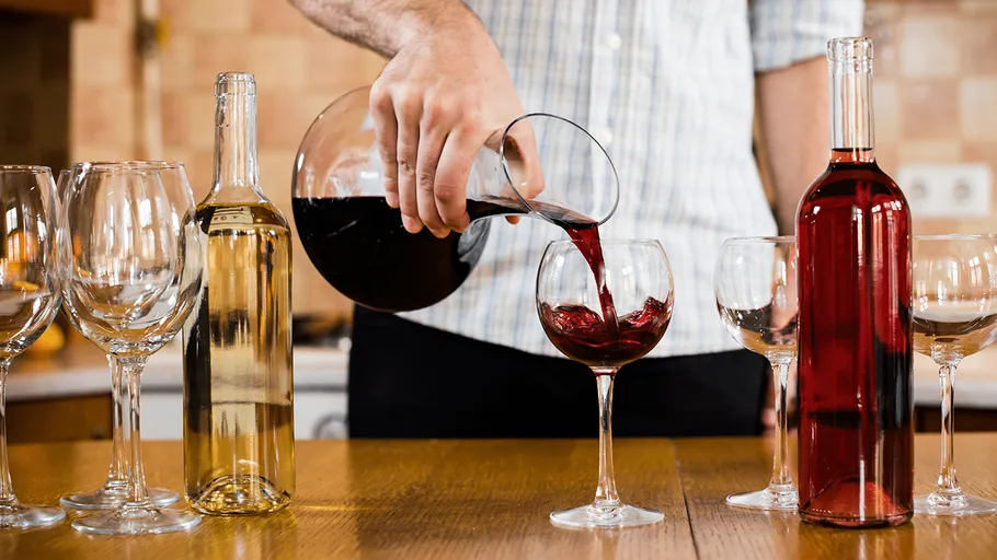 Person pouring red wine into glass on table.