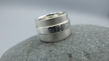 Silberner Ring mit Inschrift auf Steinoberfläche.