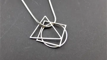 Geometrischer Silberanhänger Halskette auf dunklem Hintergrund.