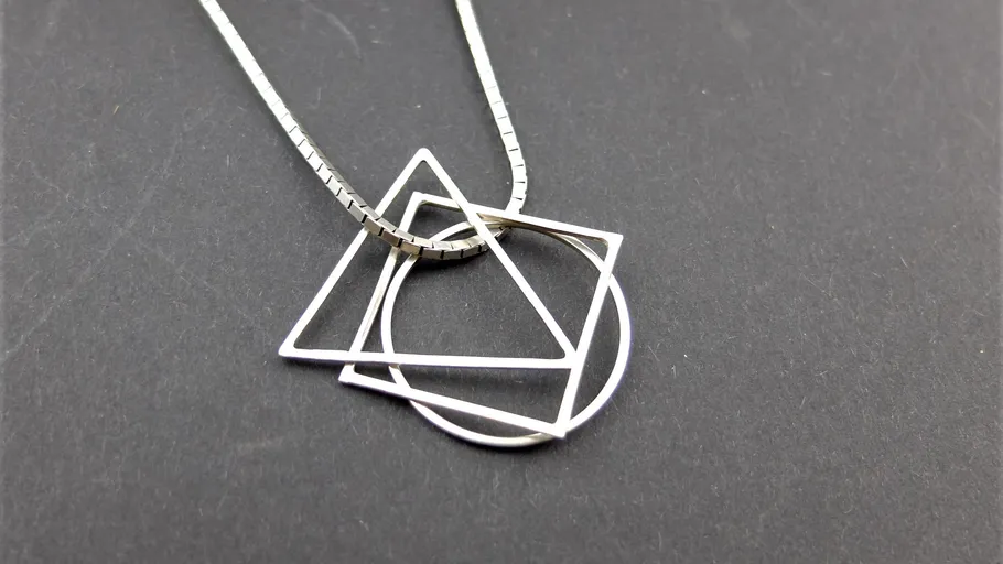 Geometric silver pendant necklace on dark background.