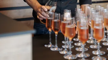 Person gießt Champagner in mehrere Gläser ein.