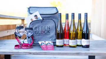 Wine bottles and gray bag on wooden table.
