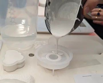 Hand gießt Flüssigkeit in Silikonform.