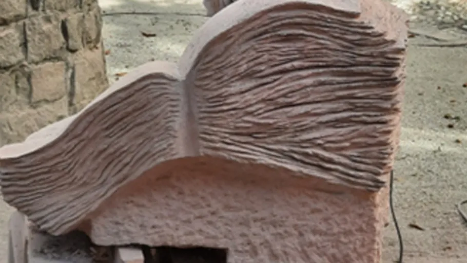 Steinskulptur mit strukturierten Linien im Freien.