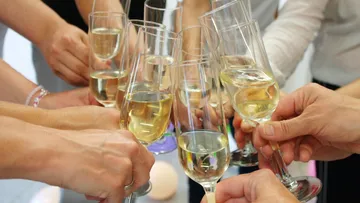 Hände stoßen mit Sektgläsern drinnen an.