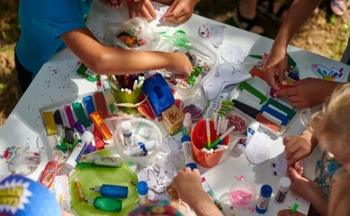 Kinder basteln mit Materialien auf einem Tisch draußen.