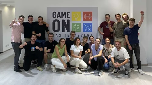 Group poses with 'Game On' sign indoors.