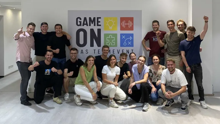 Group poses with 'Game On' sign indoors.