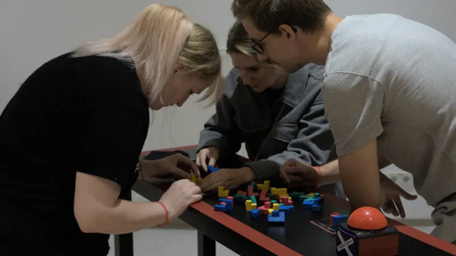 Three people assembling colorful blocks on table.