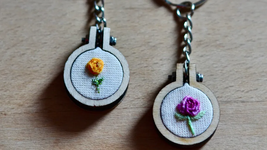 Two embroidered flower keychains on wooden surface.