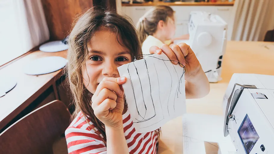 Child showing sewing project at table.