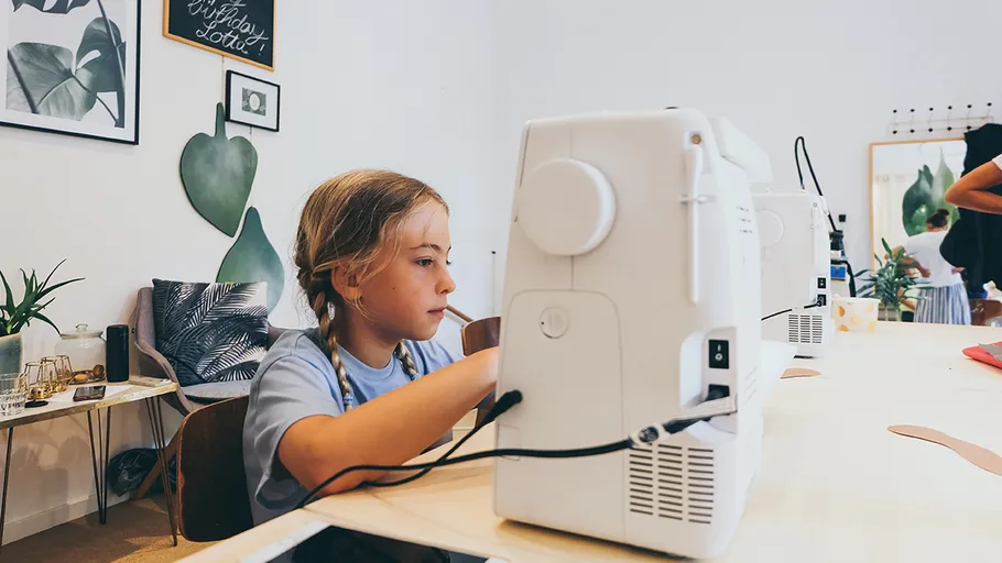 Child sewing with machine in creative room.