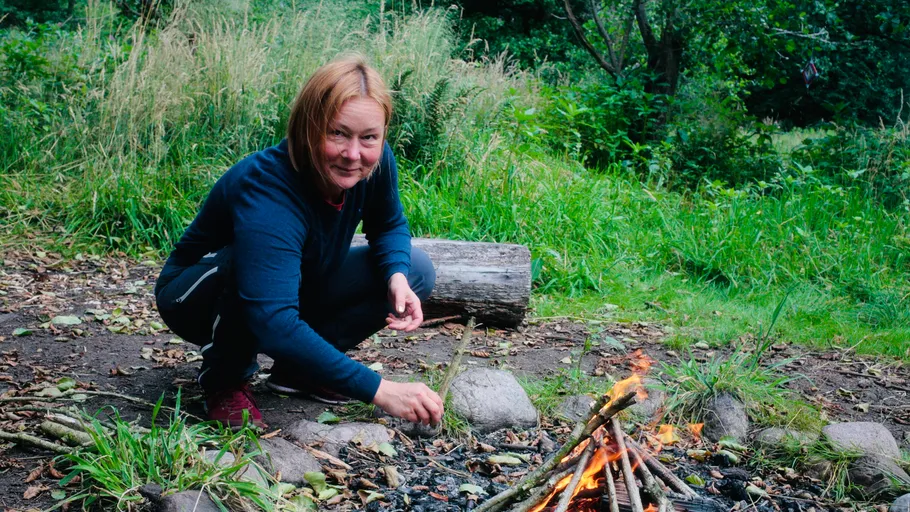 Person pflegt Lagerfeuer im Waldumfeld.