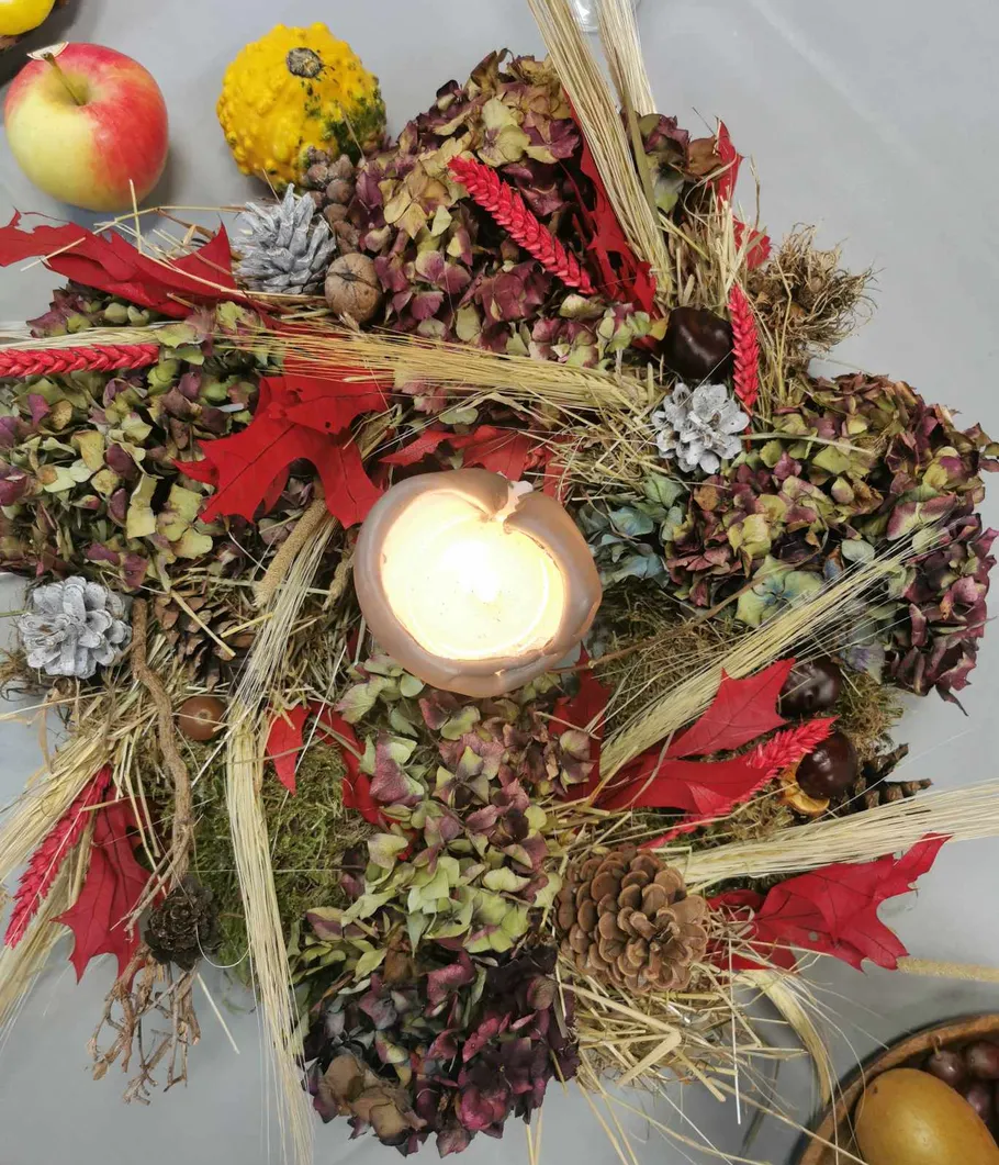 Kerze umgeben von Herbstlaub und Früchten.