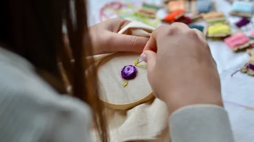 Person embroidering flower on fabric, threads nearby.