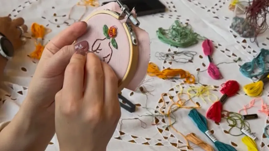 Hands embroidering cloth with colorful threads nearby.