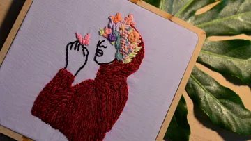 Stickerei einer Person mit Blumen und Schmetterling.