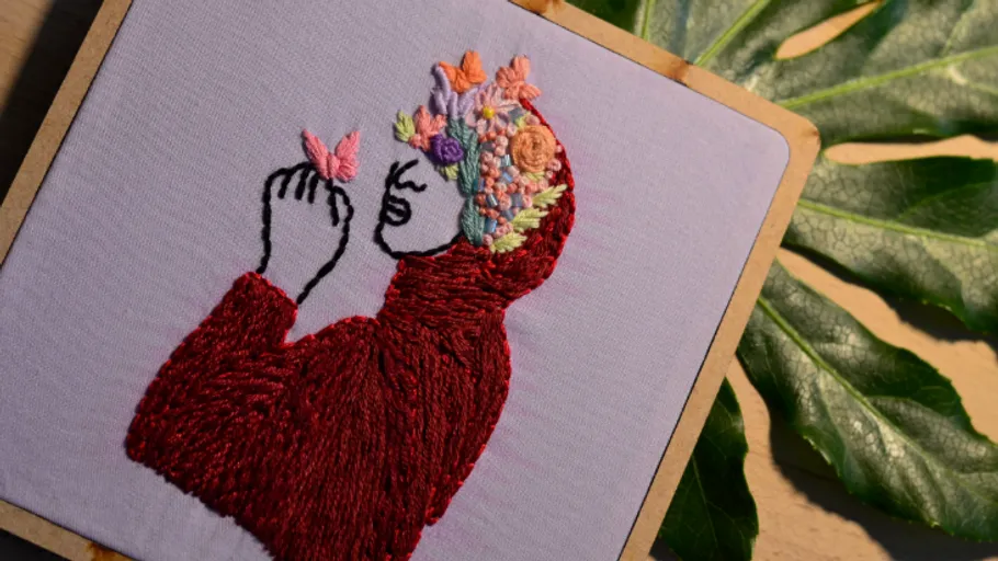 Embroidery of person with flowers and butterfly.