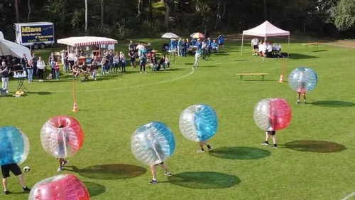 People playing bubble soccer on a grassy field.