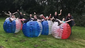 People inside inflatable balls on grassy field.