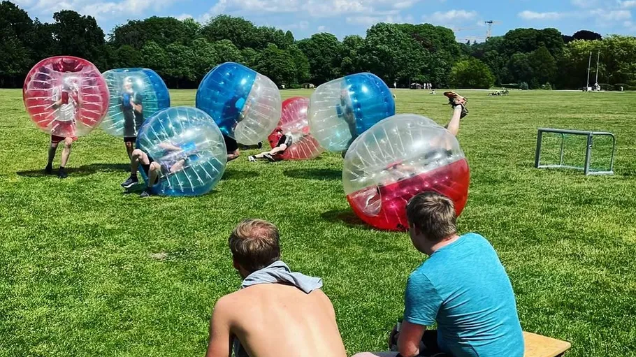 People playing bubble soccer on grassy field.