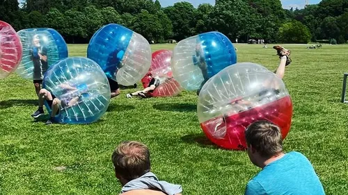 People playing in inflatable bubbles on grass.