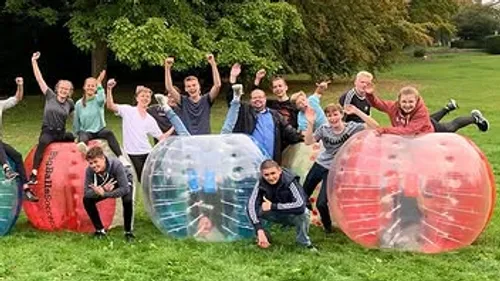 Group playing bubble soccer on grass field.