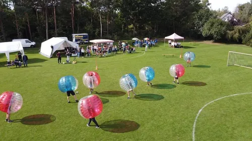 People playing bubble soccer on grass field.