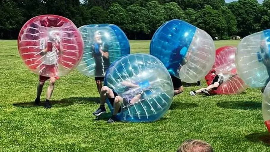 People playing bubble soccer on grassy field.