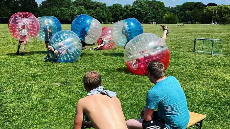 People playing bubble soccer on grass field.