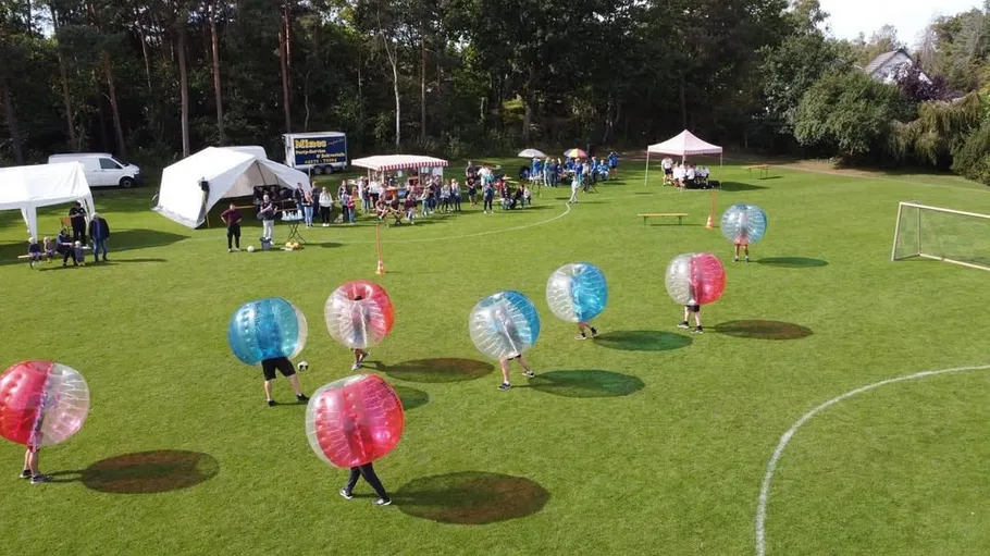 People playing soccer in inflatable bubbles outdoors.