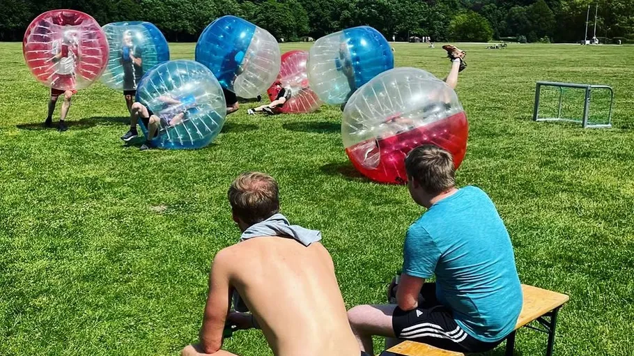 People playing bubble soccer on grassy field.