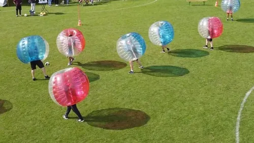 People playing bubble soccer on grass field.